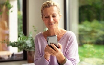 Middle aged woman looking at phone with garden in the background