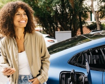 Smiling woman charging her electric car and using her phone