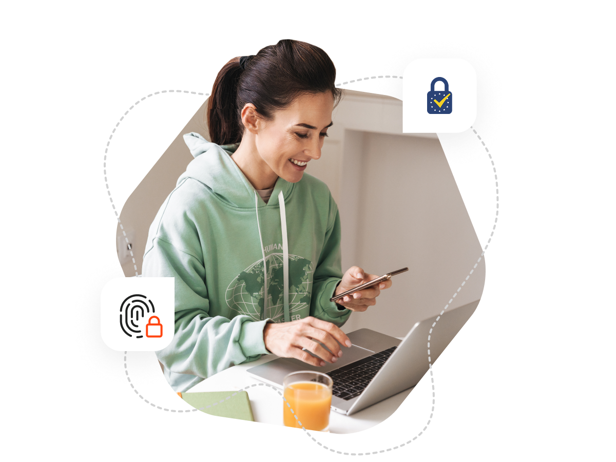 A woman sitting at her table with her laptop open in front of her, she is also looking at her phone