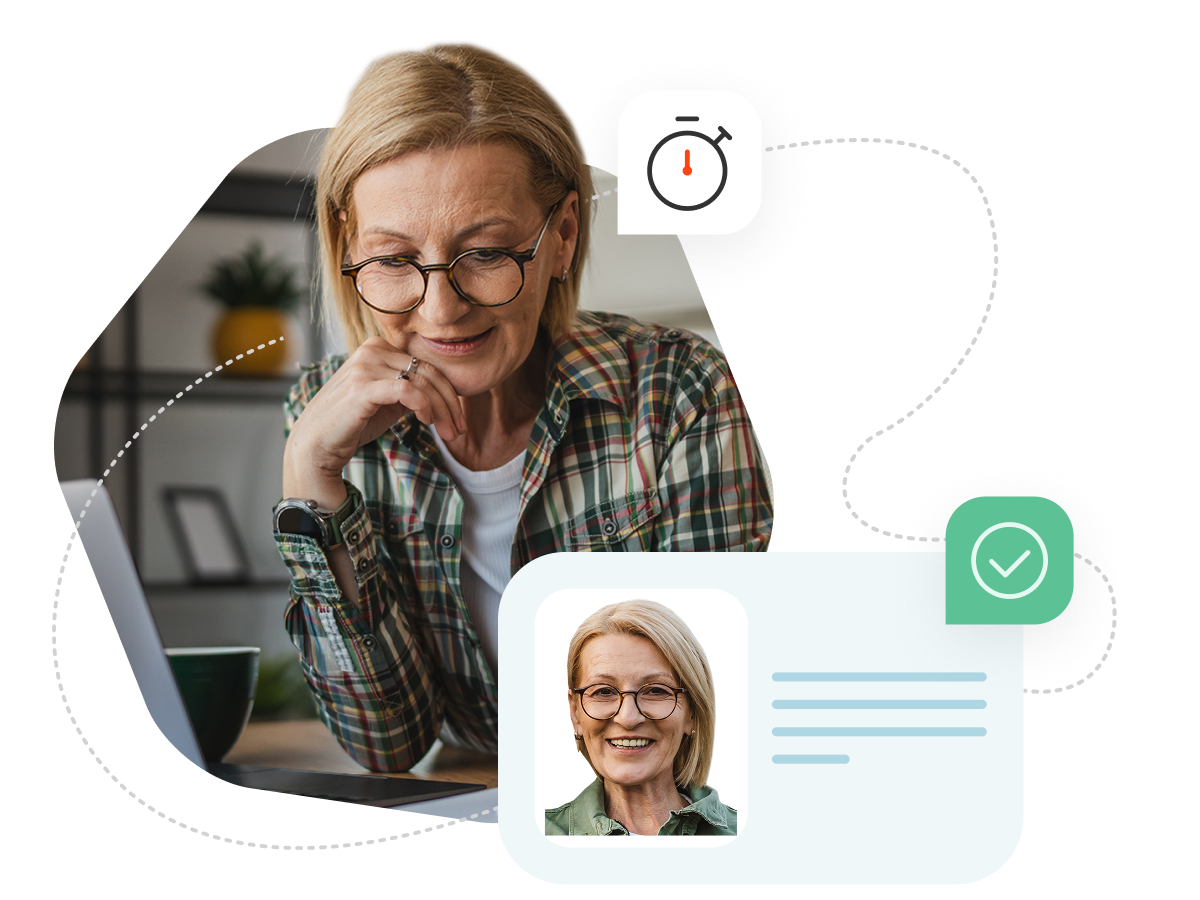 A woman with short hair and round glasses is standing next to a kitchen counter looking at her laptop